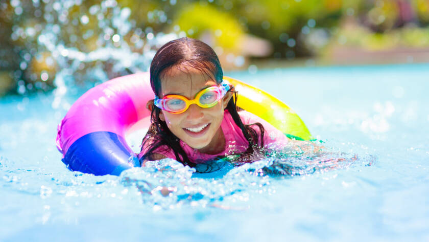 Child in swimming pool floating on toy ring. Kids swim. Colorful rainbow float for young kids. Little boy having fun on family summer vacation in tropical resort. Beach and water toys. Sun protection.