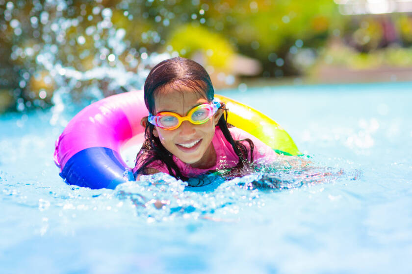 Child in swimming pool floating on toy ring. Kids swim. Colorful rainbow float for young kids. Little boy having fun on family summer vacation in tropical resort. Beach and water toys. Sun protection.