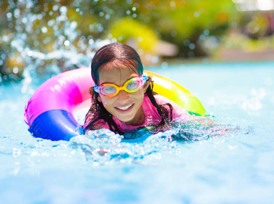 Child in swimming pool floating on toy ring. Kids swim. Colorful rainbow float for young kids. Little boy having fun on family summer vacation in tropical resort. Beach and water toys. Sun protection.